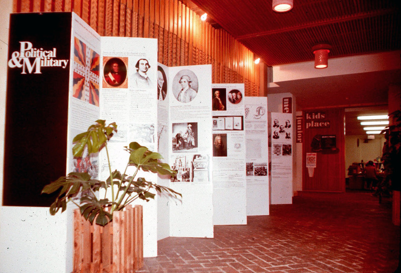 In addition to the exhibit, there are many things going on in this photograph of importance. First of all, this is one of the few photographs that capture the Mexican brick flooring that was in the 1968 addition to the library. It was made by Acme Brick Co. for O'Neil Ford and was called "el Fordo". The wall of chip carvings was made by Lynn Ford, brother of O'Neil Ford and well-known for his woodcarvings and metal work.