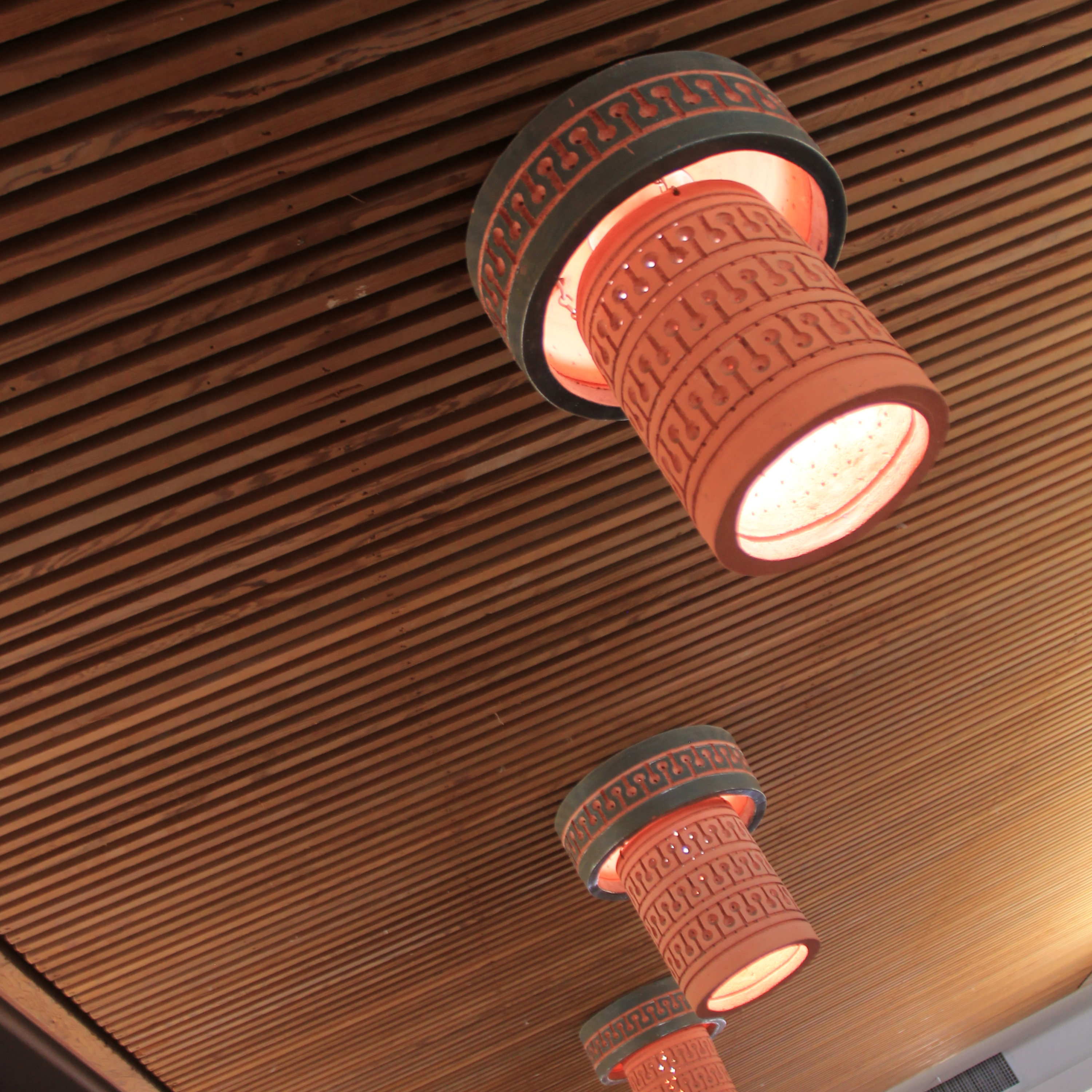 Ten Beaumont Mood flush-mount ceramic lights hang from a suspended ceiling. They are a salmon color with an "elephant blue" band at the top. 