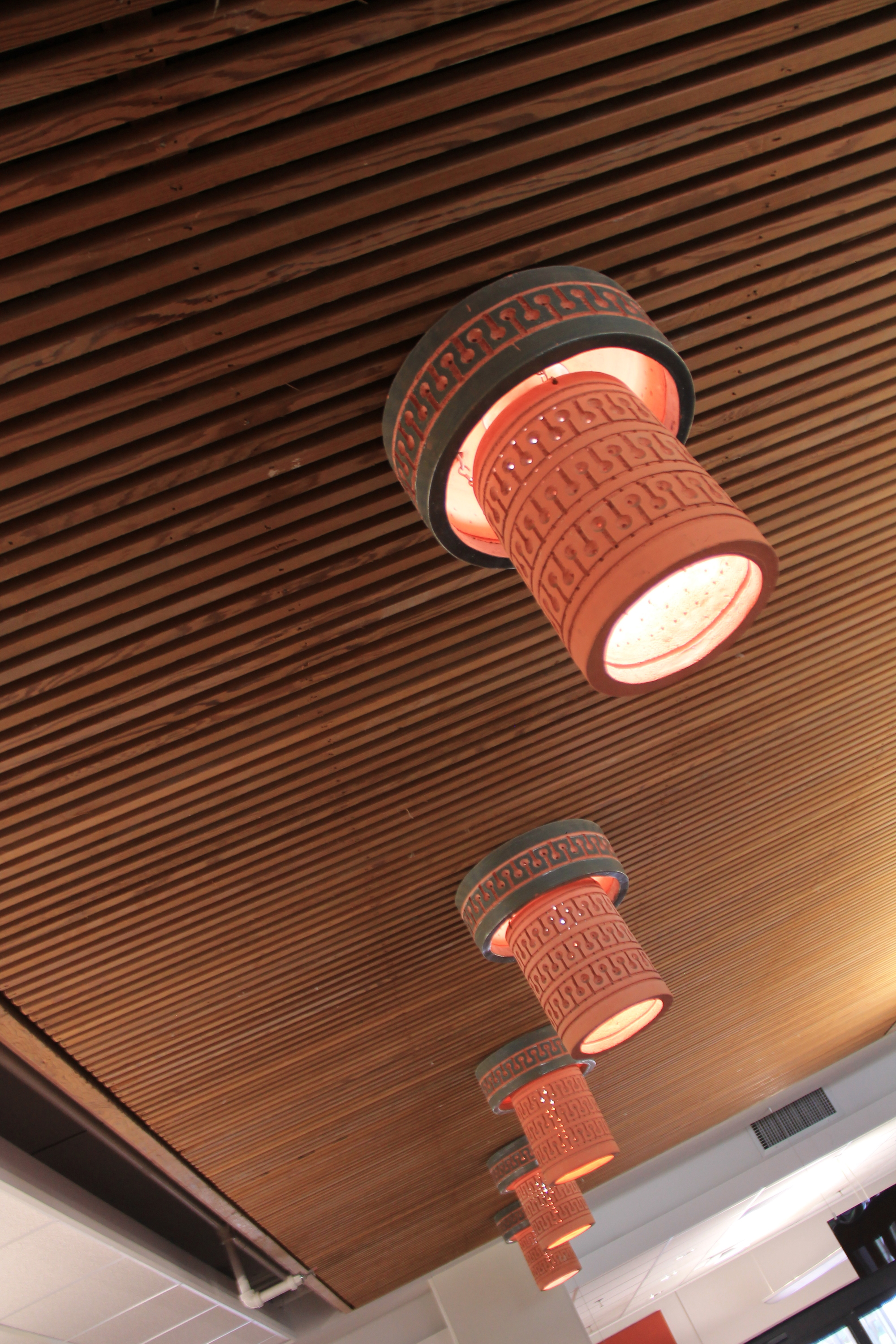 Ten Beaumont Mood flush-mount ceramic lights hang from a suspended ceiling. They are a salmon color with an "elephant blue" band at the top. 